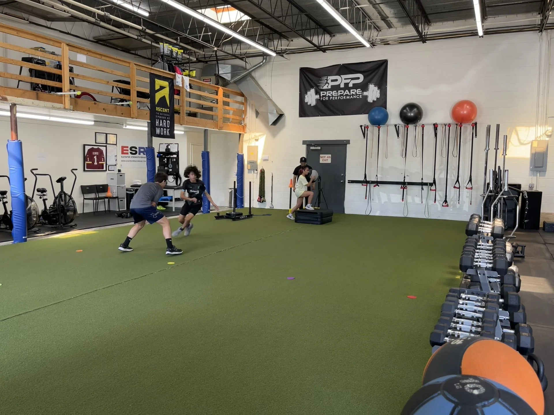 Children practicing soccer in an indoor gym with gym equipment and exercise balls on the wall